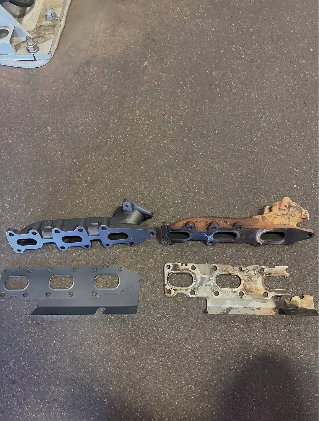 The old warped exhaust manifold and burnt gasket next to the clean updated replacement